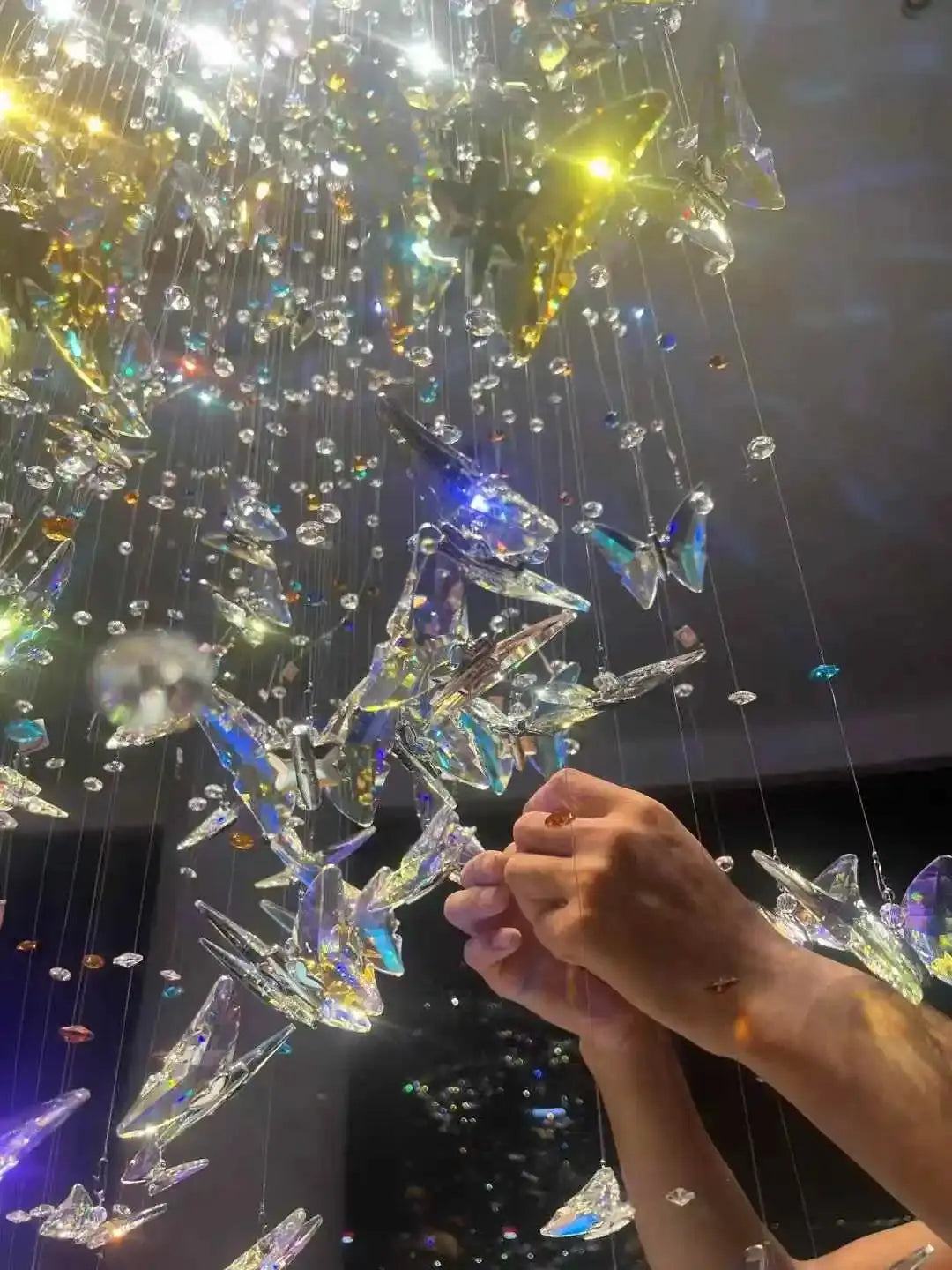 Hand touching a sparkling chandelier with multicolored crystals