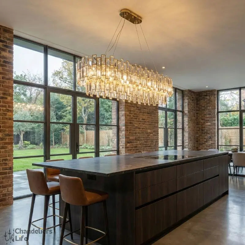 Modern kitchen with a large island and chandelier, featuring a brick wall and large windows.