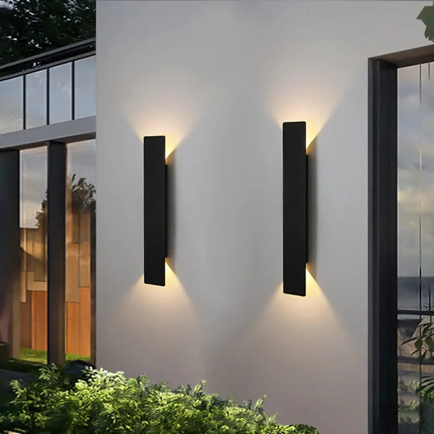 Two modern outdoor wall lights on a building exterior with greenery.