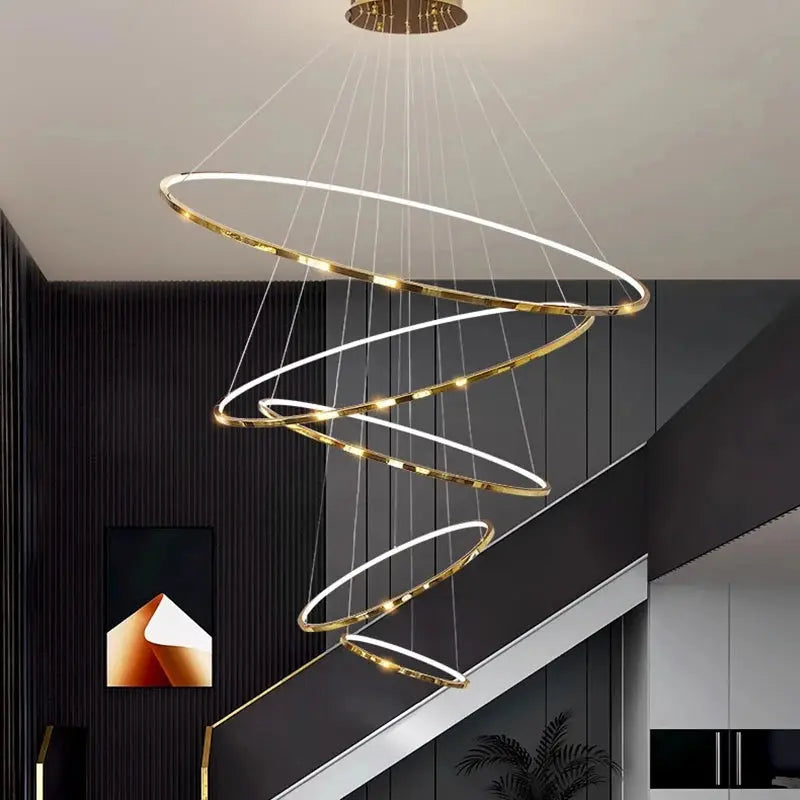 Modern chandelier with gold and white rings hanging in a room with dark walls and a staircase.