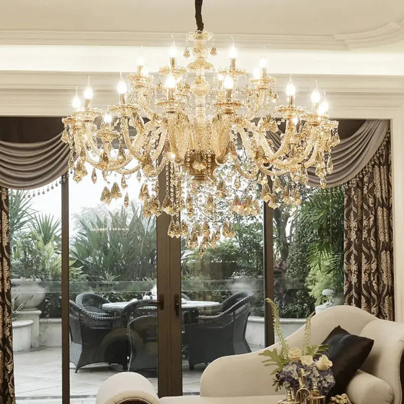 A sparkling crystal chandelier with a modern design, hanging in a room with a curtain and a window view of lush greenery.